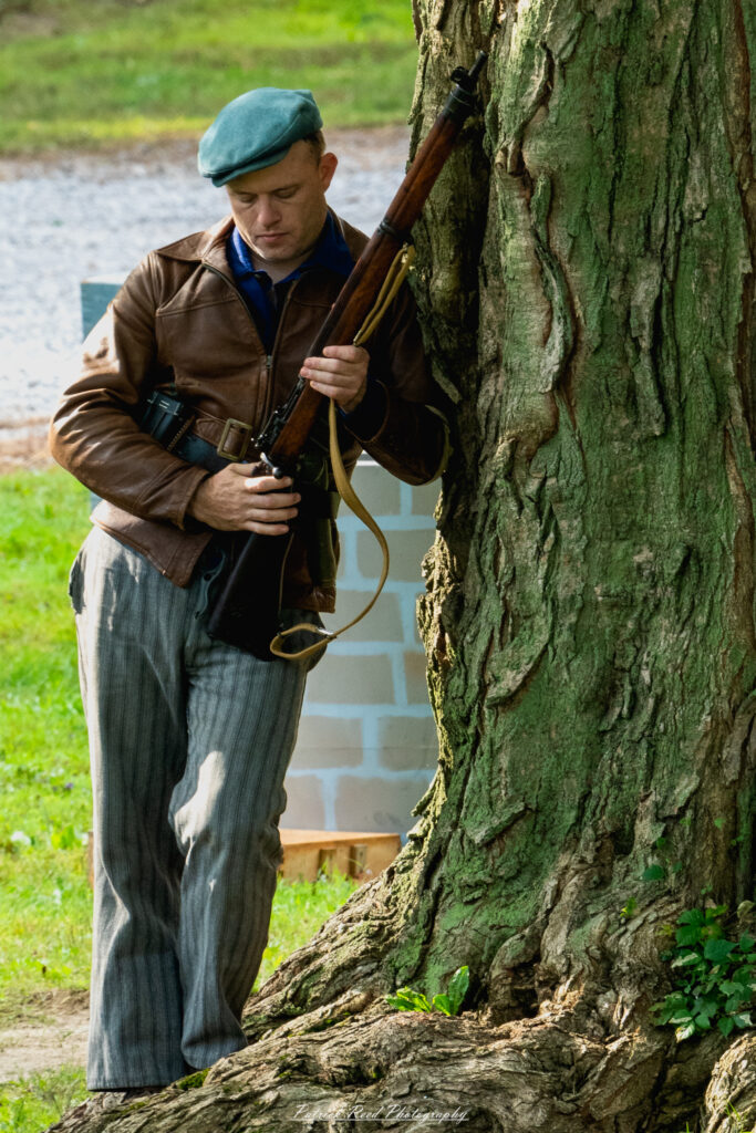 "A vivid portrayal of a French Resistance soldier leaning against a tree, clutching a rifle. The image captures a moment of tense vigilance, with the soldier's determined expression reflecting the courage and resolve of the Resistance fighters during WWII."